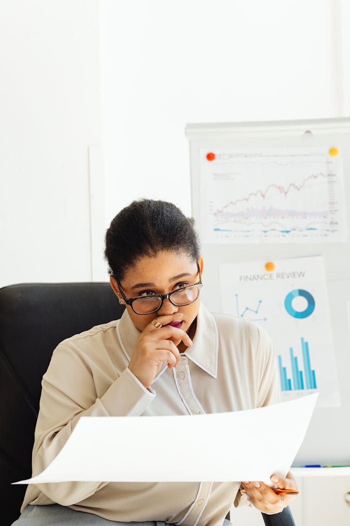 Woman analyzing financial charts with whiteboard in office, illustrating focus and strategy.